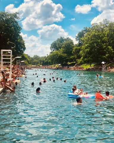 Barton Springs Pool packed with swimmers and floaties under a vivid blue sky