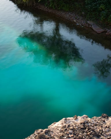 Turquoise water with limestone rock edge and tree reflections, natural swimming hole
