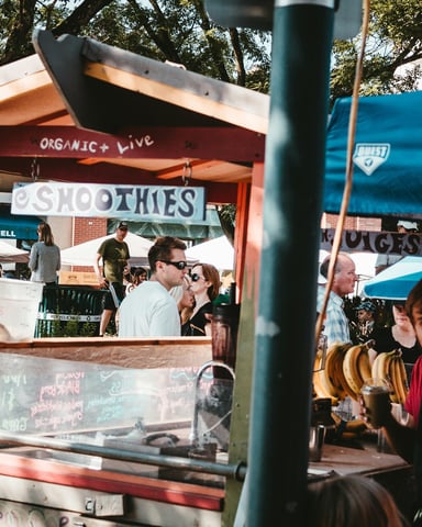 Outdoor food market with a smoothie stand and lively crowd under trees in Austin