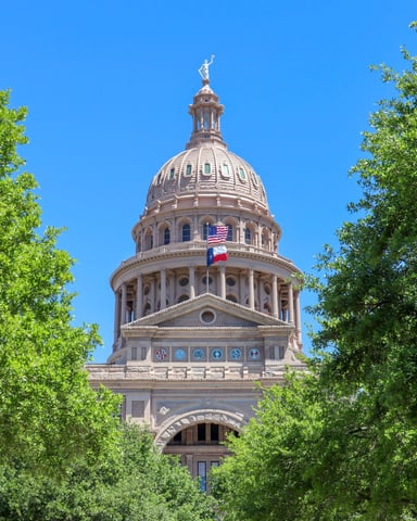 Texas State Capitol dome framed by lush green spring trees against a vivid blue sky