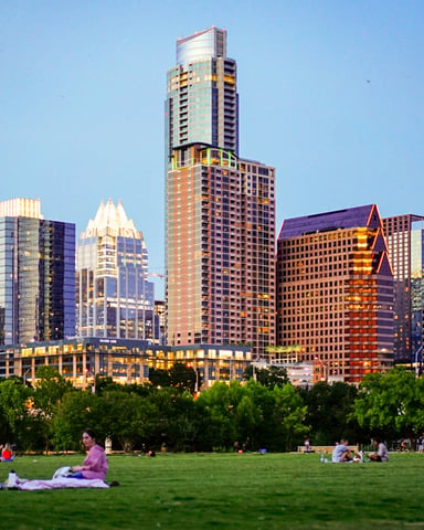 People relaxing on the green lawn at Auditorium Shores with the Austin skyline glowing at dusk