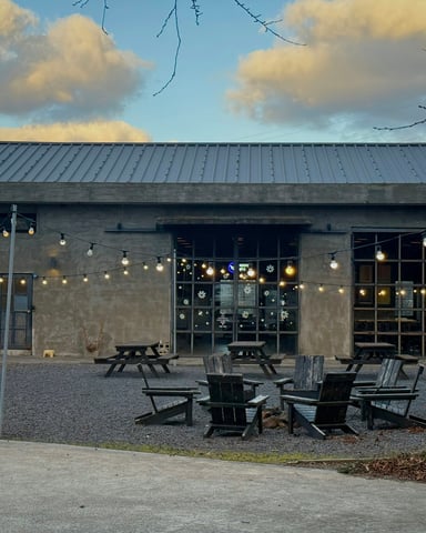 Industrial brewery building exterior with string lights and Adirondack chairs on a gravel patio