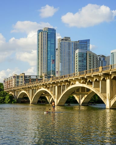 Paddleboarder on Lady Bird Lake with the Congress Avenue bridge and Austin skyline