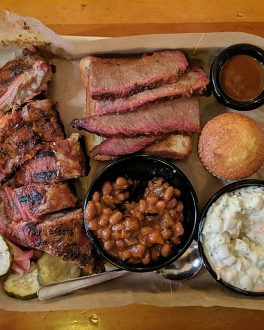 Full Texas BBQ tray with brisket, ribs, beans, coleslaw, and cornbread