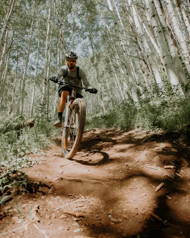 Mountain biker riding a red dirt trail through bright aspen trees