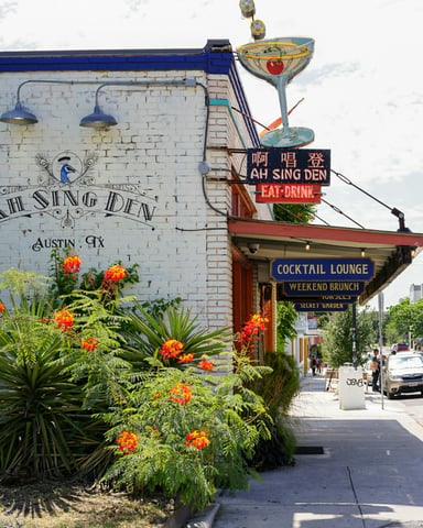 Ah Sing Den cocktail lounge on an Austin street, colorful neon signs and orange tropical flowers