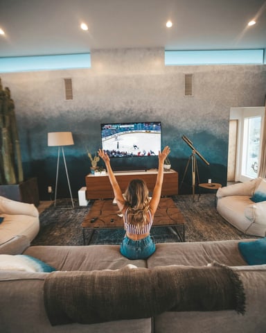 Woman with arms raised watching a hockey game on a large flat-screen TV in a vacation home