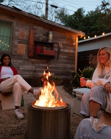 Friends gathered around a glowing firepit with string lights on a warm Texas evening