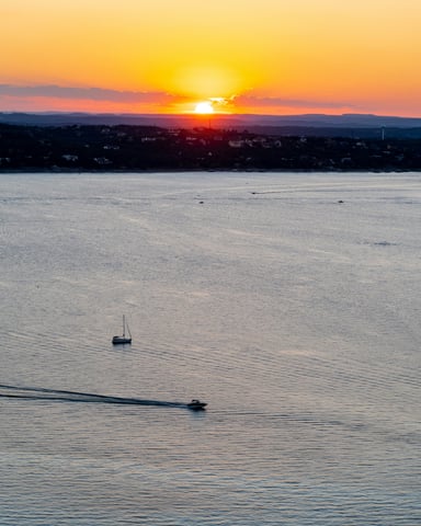 Sailboat and motorboat on Lake Travis at sunset with orange sky reflecting on the water