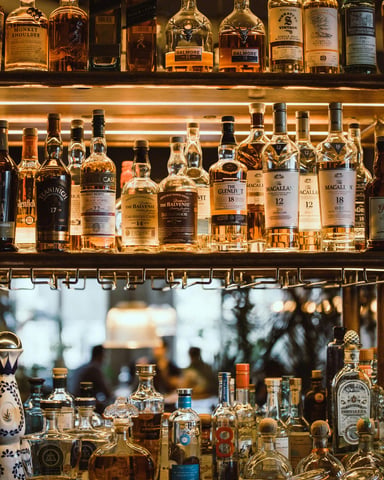 Two backlit shelves packed with whiskey and spirits bottles at a bar, warm amber glow