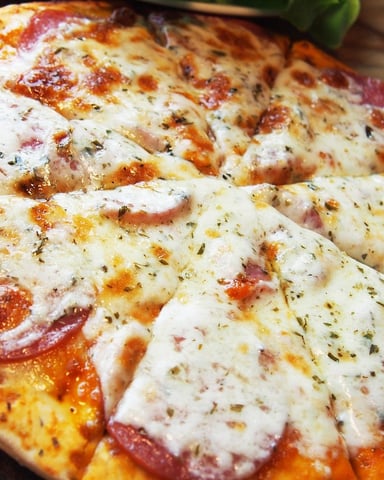 Pepperoni and mozzarella pizza with herbs on wooden table