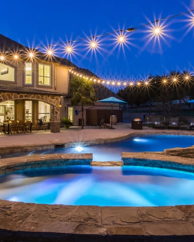 Stone pool and hot tub glowing blue at night with string lights overhead