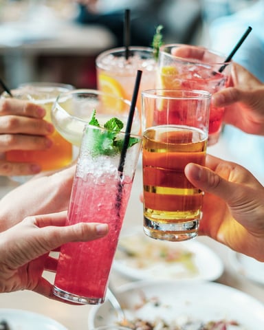 Group of people toasting with colorful cocktails and drinks at an outdoor table