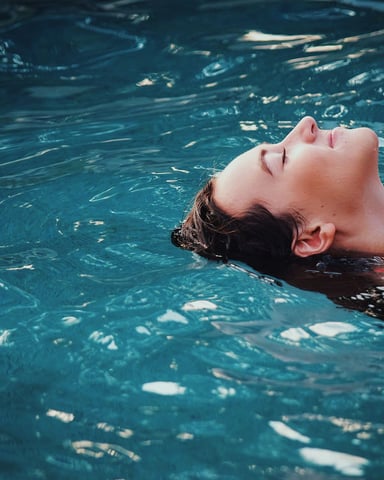 Person floating on back in clear blue swimming pool water