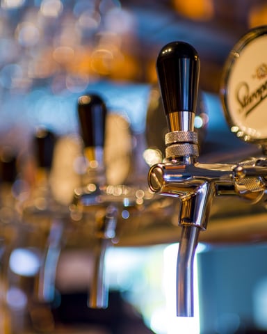 Close-up of polished beer tap handles with branded drum head at bar counter, evening lighting