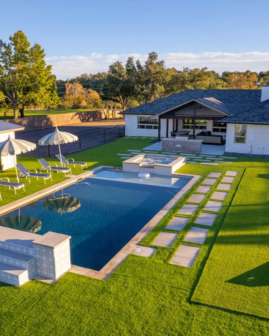 Aerial view of white ranch house with rectangular pool, sun loungers, and wide green lawn