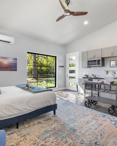 Bright Dripping Springs studio with king bed, kitchenette, and garden view through black-frame windows