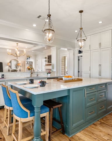 Spacious kitchen with white cabinetry, teal island with marble countertop, blue upholstered chairs, pendant lights, and stainless steel appliances.