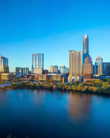 Downtown skyline with tall buildings and river at sunset, green trees along waterfront