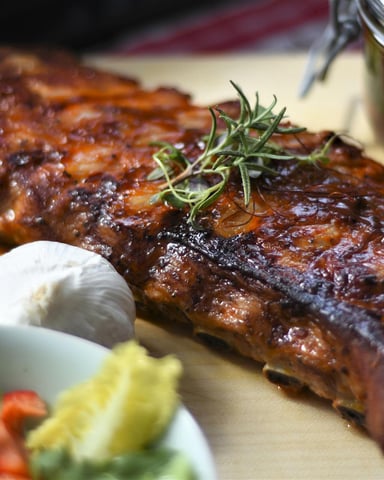 Glazed ribs with rosemary garnish, sour cream, and sauce on wooden board