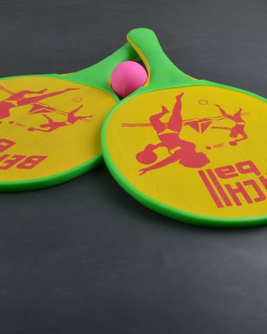 Green and yellow paddle rackets with red graphics and a pink ball on gray background