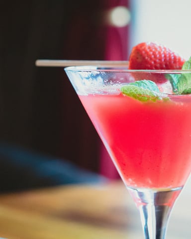 Red cocktail in martini glass garnished with fresh strawberry and mint leaves