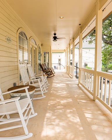 Wide wraparound porch with rocking chairs under live oak trees