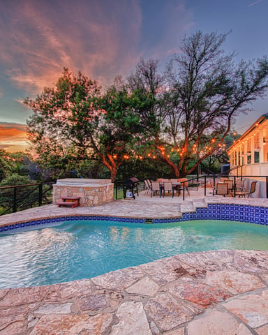 Backyard pool with blue tile at sunset, stone patio, fire pit, dining area, and modern house with valley views