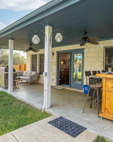 Covered patio with outdoor bar seating, ceiling fans, and green lawn beyond