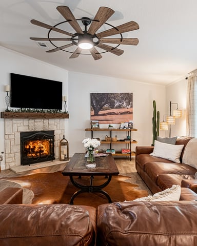 Open-plan living room with fireplace, wood stove, leather seating, and ceiling fan with wood blades