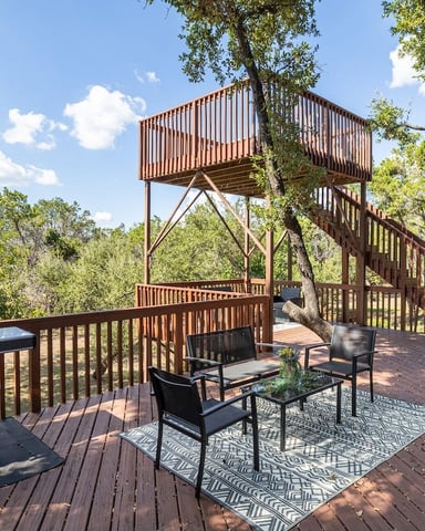 Wooden deck with grill, seating area, and elevated tower structure surrounded by tall trees