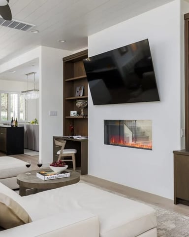 Spacious open-concept living room with fireplace, large TV, and kitchen visible in the background