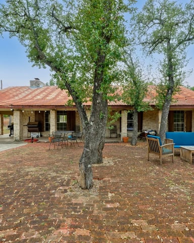 Hill Country ranch exterior with live oak trees and outdoor seating