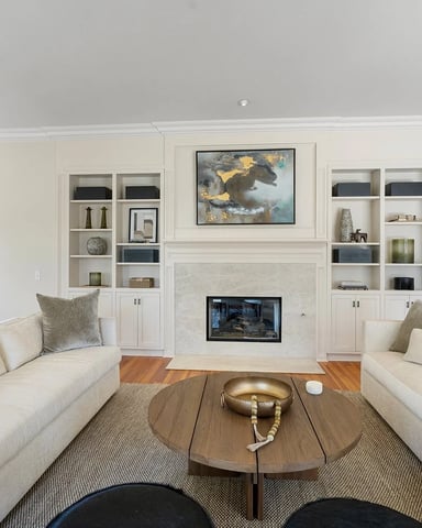 Formal living room with two cream sofas facing a fireplace, built-in shelving, and hardwood floors