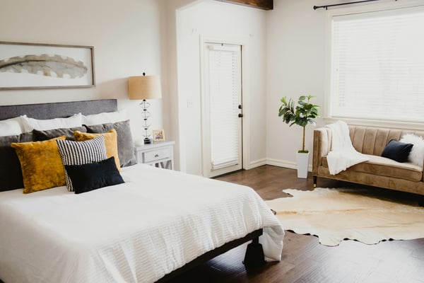 Warm vacation rental bedroom with cowhide rug, mustard pillows, dark hardwood floors, and natural light