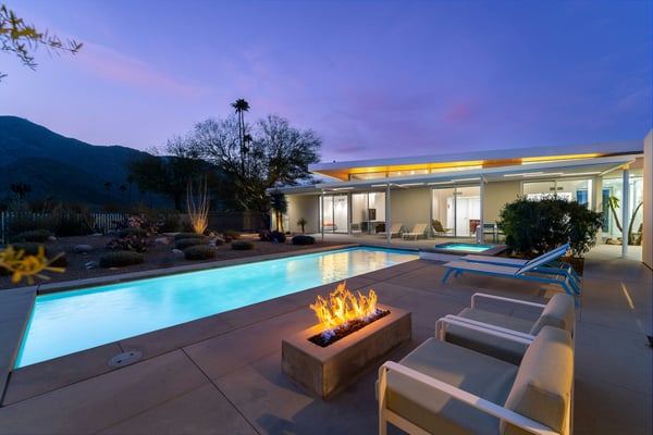 Luxury home at blue hour with glowing pool, fire pit, lounge chairs, and mountain backdrop