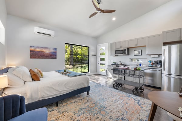 Bright, well-appointed studio bedroom with a king bed, kitchenette, and large window looking out to a green garden