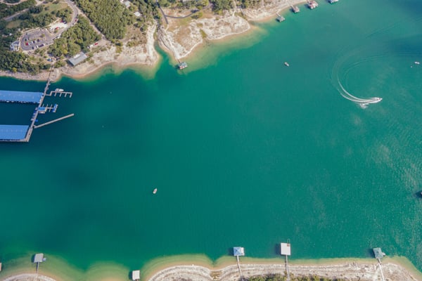 Aerial view of Lake Travis with vivid teal water, boat docks, and sandy shoreline